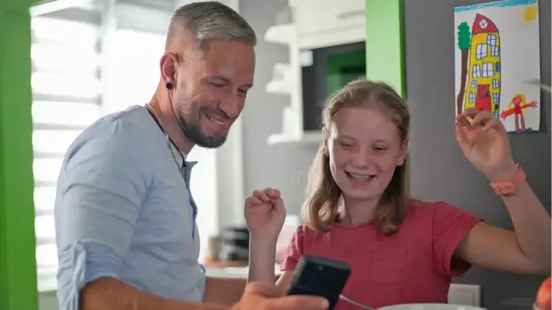 Zwei Personen schauen auf ein Smartphone und freuen sich.